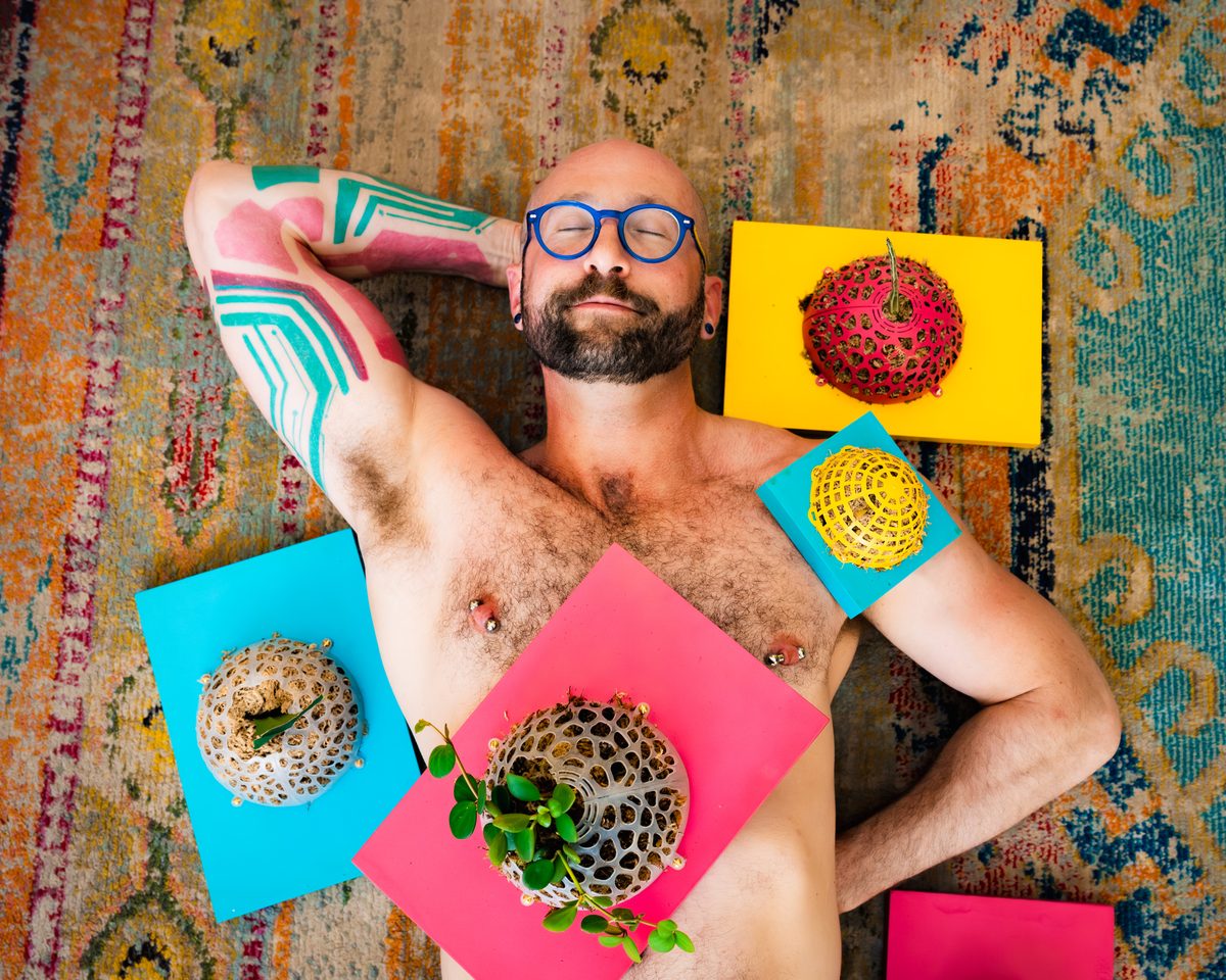A muscled and tattooed man with plants draped over him